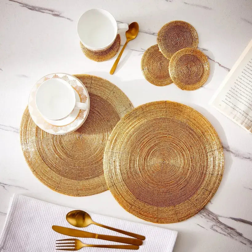 Woven placemats and coasters on a marble surface with gold cutlery.
