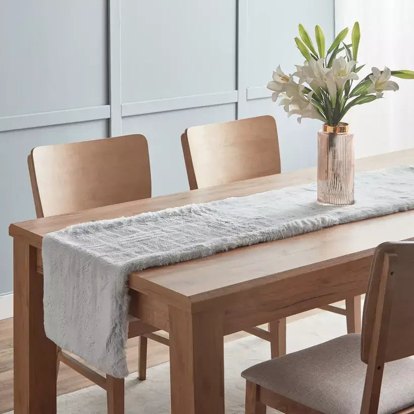 Dining table set with chairs and a gray runner, featuring a vase with white flowers.