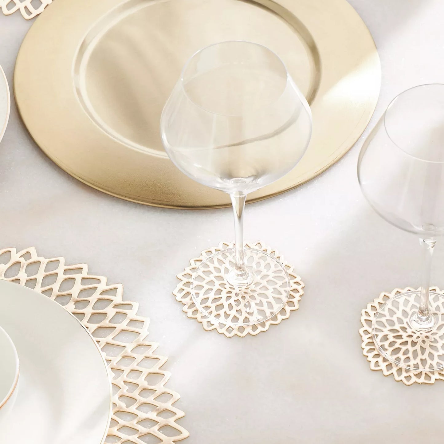 Table setting with gold plates, glasses, and decorative coasters on a white surface.