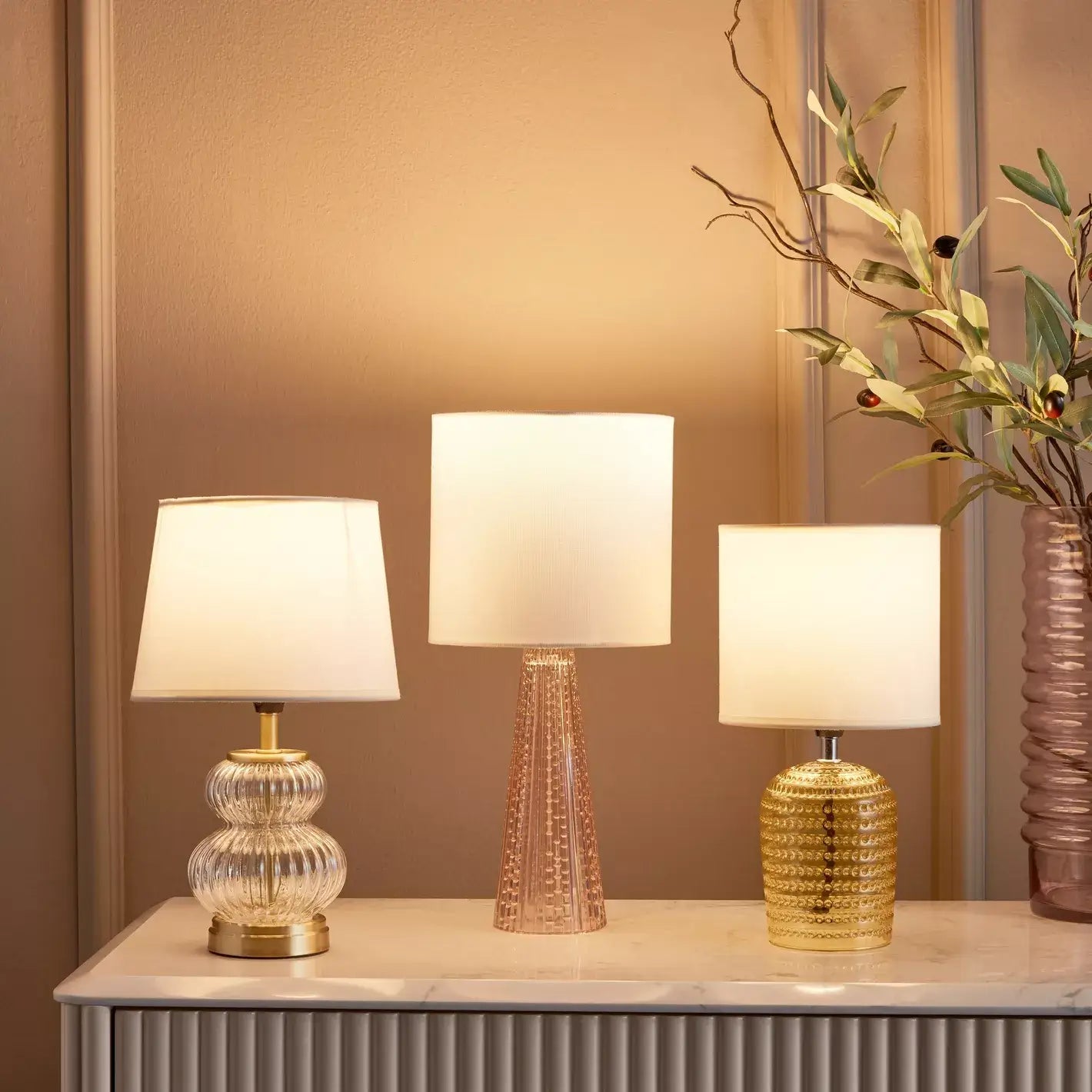 Three table lamps with textured bases on a wooden surface against a beige wall.