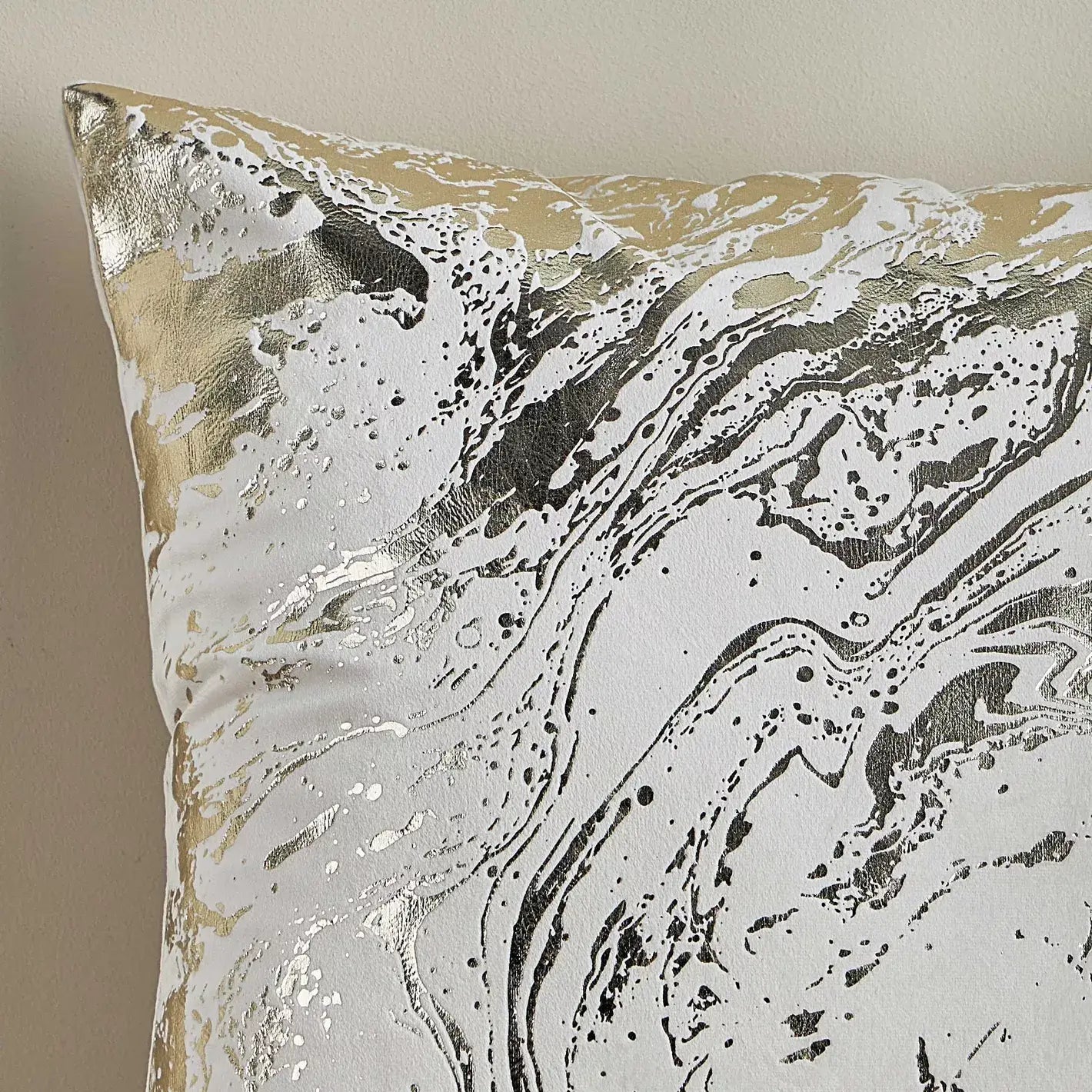 Decorative pillow with marble-like pattern in gold, black, and white on a beige background