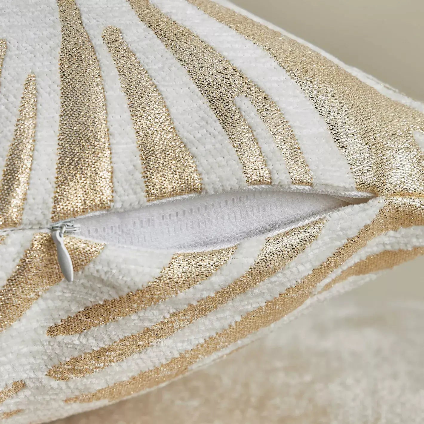 Close-up of a decorative pillow with gold and white leaf patterns on a neutral background.