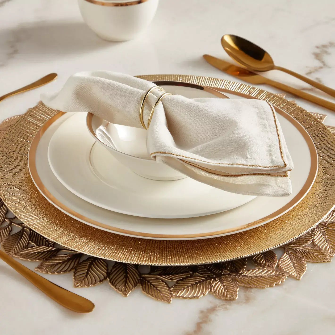 Elegant table setting with gold and white plates, napkin, and cutlery on a marble surface.