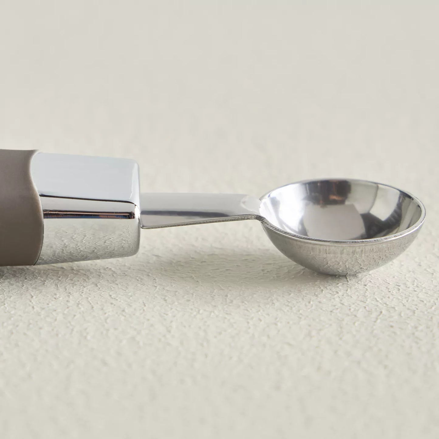 Metallic ice cream scoop on a light beige background