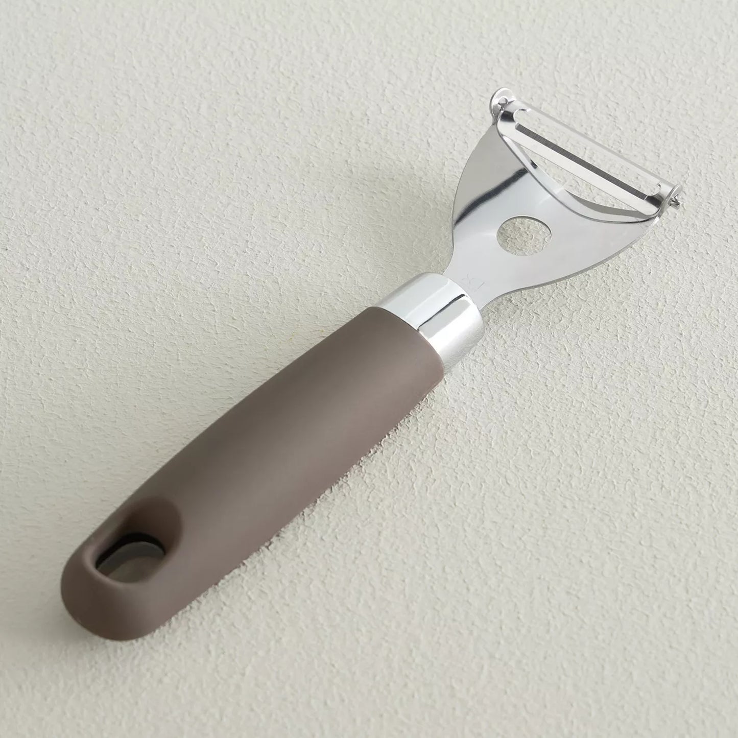 Peeler with brown handle and silver blade on a light gray background