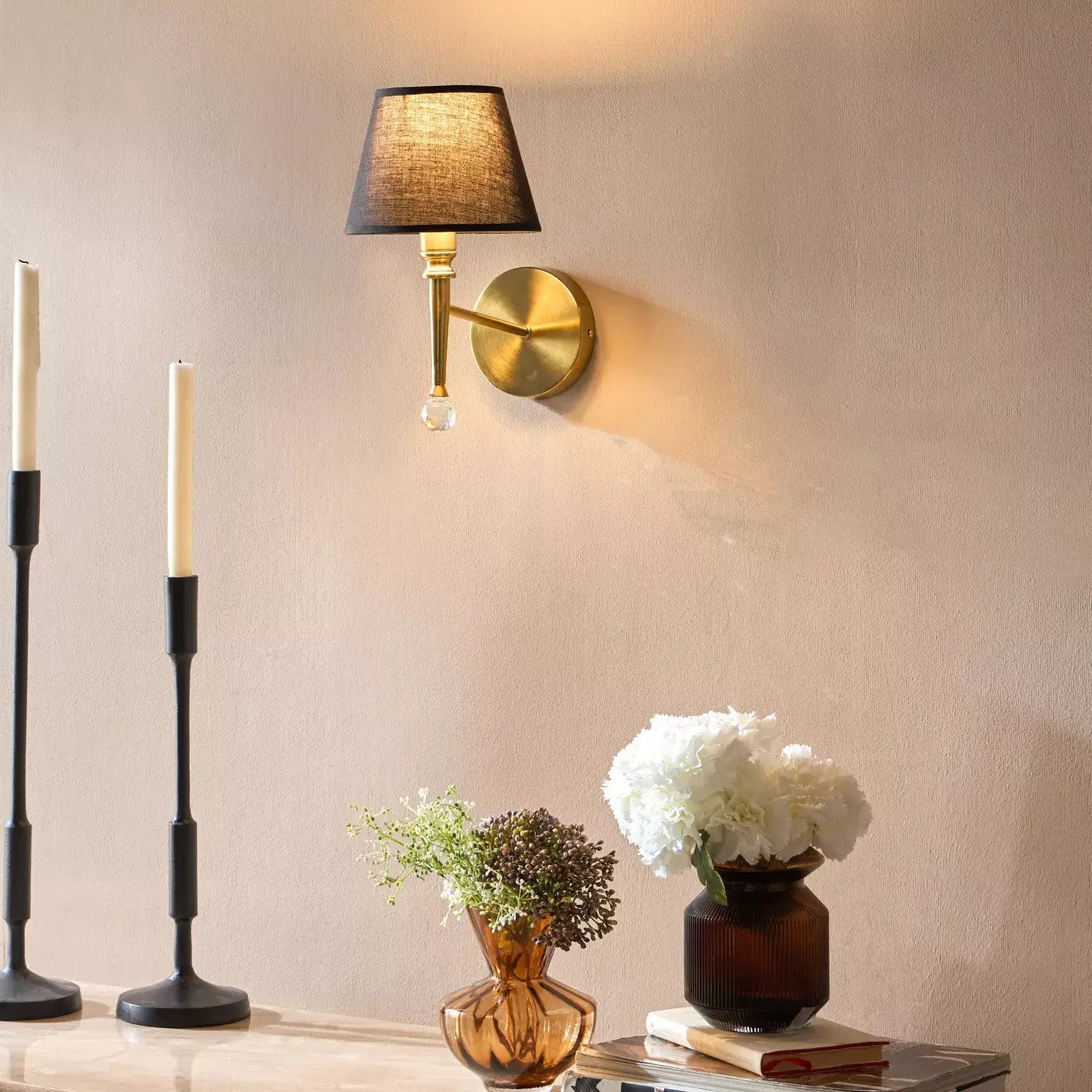 Wall-mounted lamp with candles and decorative vases on a table against a beige wall.