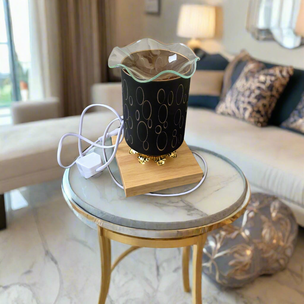 A small electric oil warmer with a glass container on a wooden base, plugged into a wall socket.