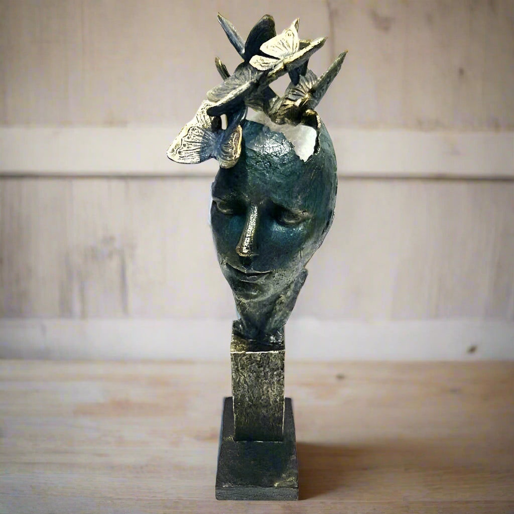 Bronze sculpture of a face with butterfly wings on a wooden surface