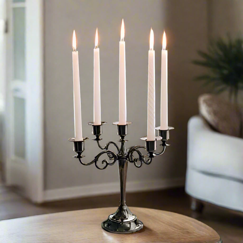 Candle holder with lit candles on a wooden table, with a vase and plant in the background.
