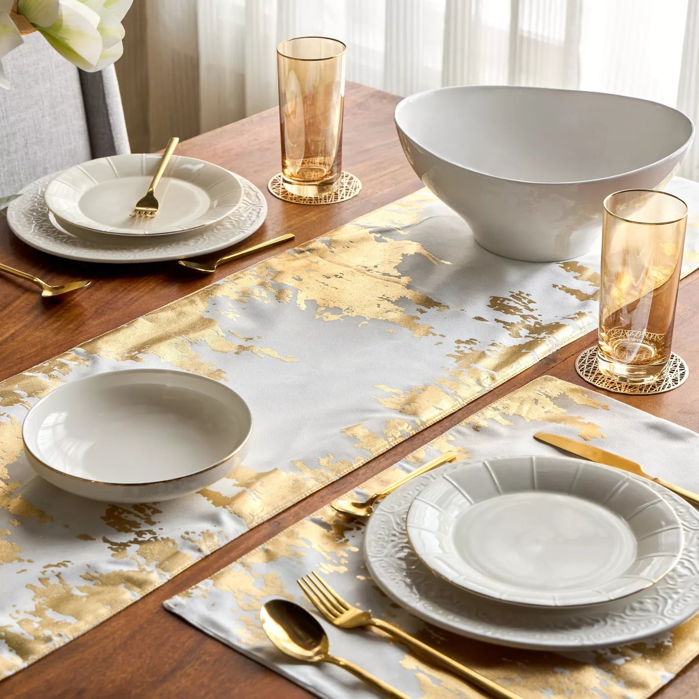 Dining table setting with white plates, gold cutlery, and a gold and silver patterned placemat.