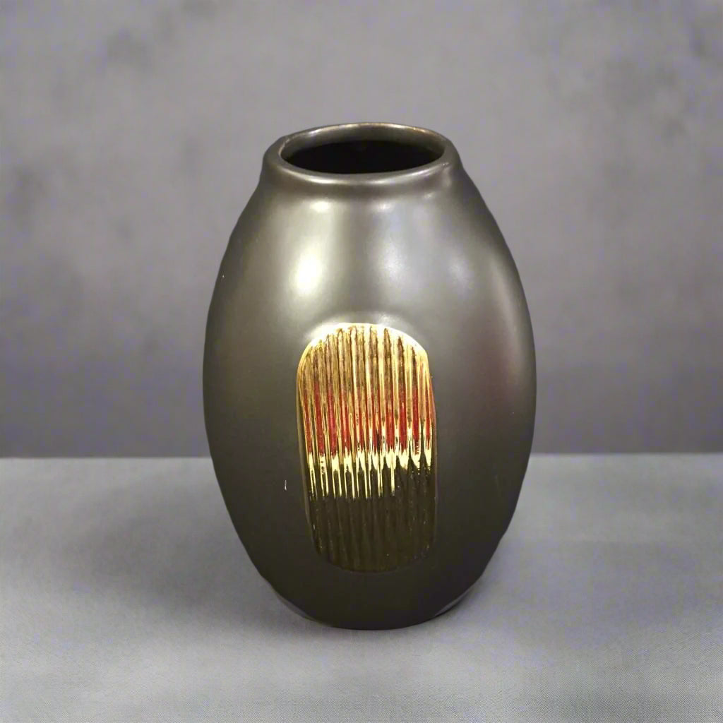 A round black ceramic vase with a textured gold accent on a dark background.