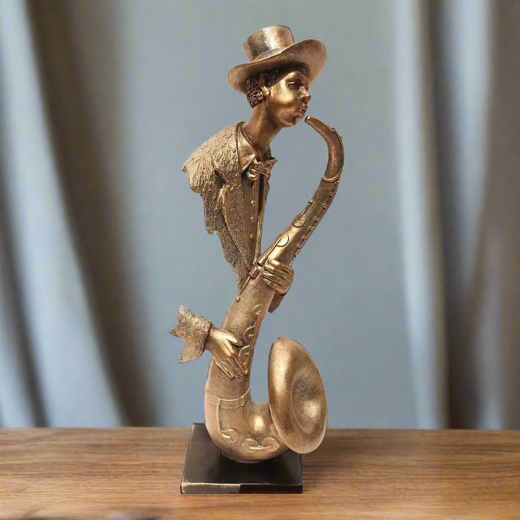 Bronze sculpture of a musician playing a saxophone on a wooden surface with a blurred curtain background.
