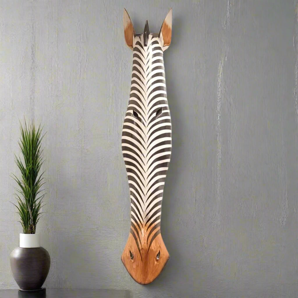 Wooden zebra head wall decoration on a gray wall with a plant beside it.