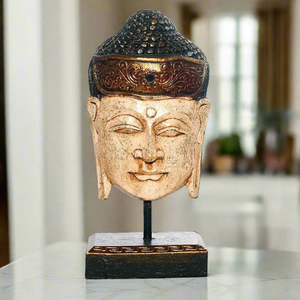 Statue of a Buddha head on a stand with a blurred indoor background