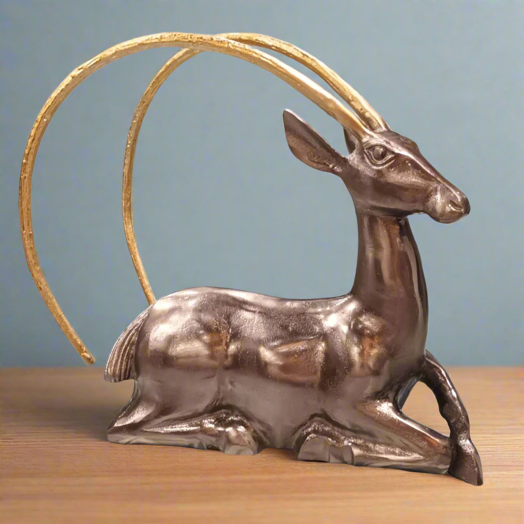 Metallic deer figurine with a gold antler on a wooden surface and blue background