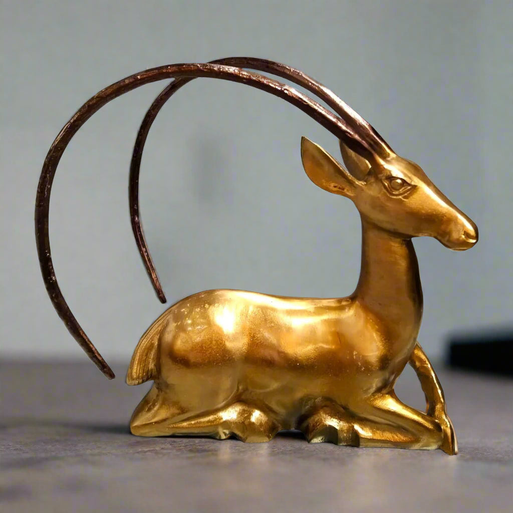 Gold antelope figurine with long horns on a gray background