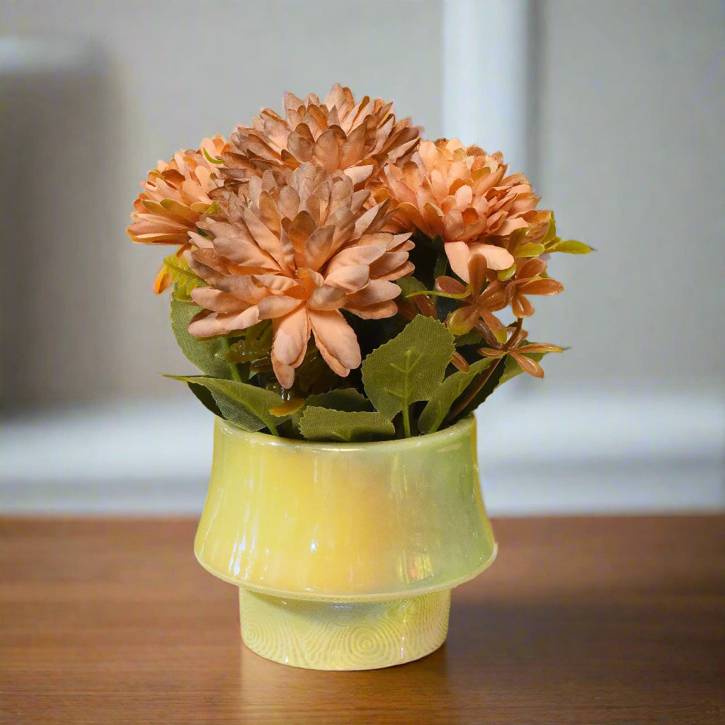 Artificial flower arrangement in a green vase on a textured surface with a yellow background