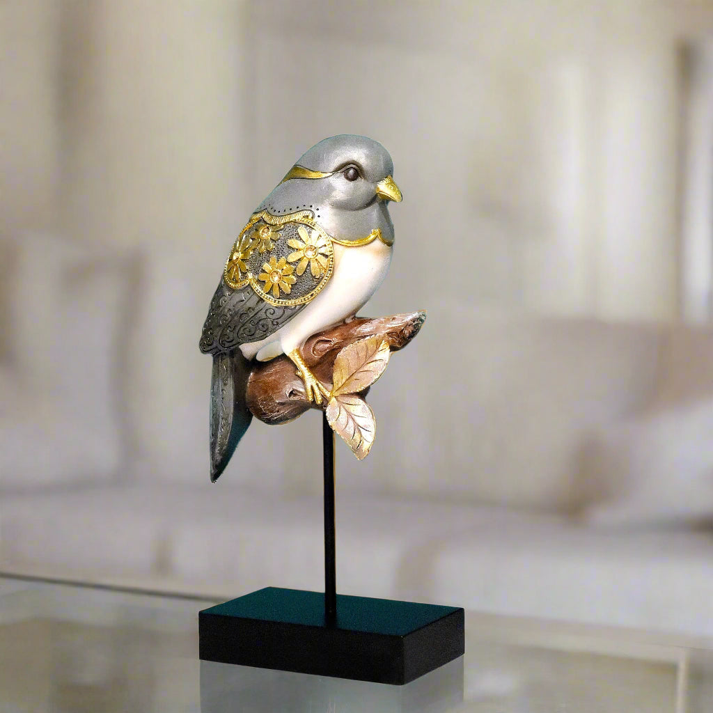 Decorative bird sculpture with gold accents on a stand in a blurred indoor setting