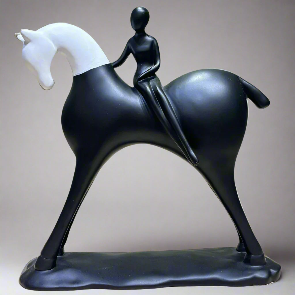 Black and white sculpture of a horse with a rider on a wooden surface and green background