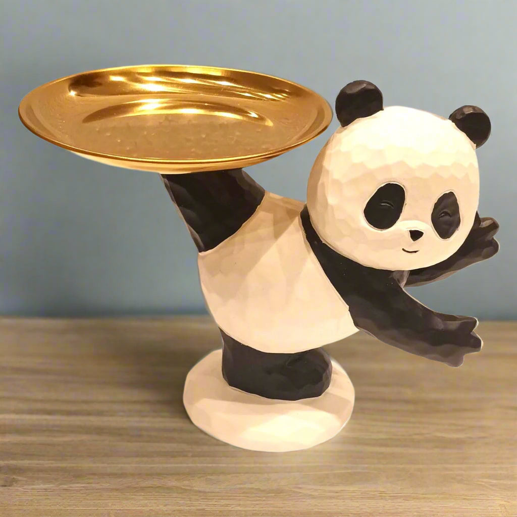 Panda figurine holding a gold plate on a wooden surface with a light blue background