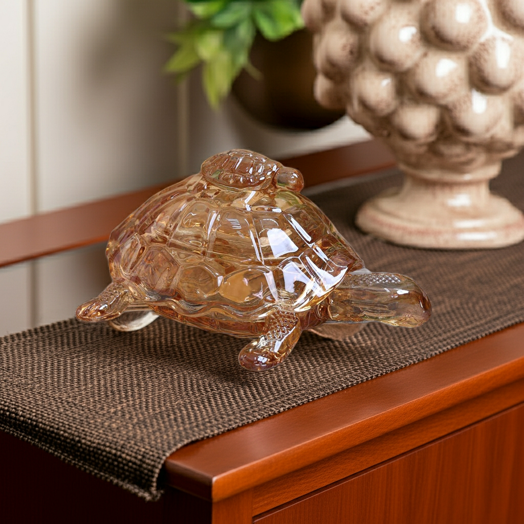 Glass turtle figurine on a wooden surface with a plant and decorative item in the background