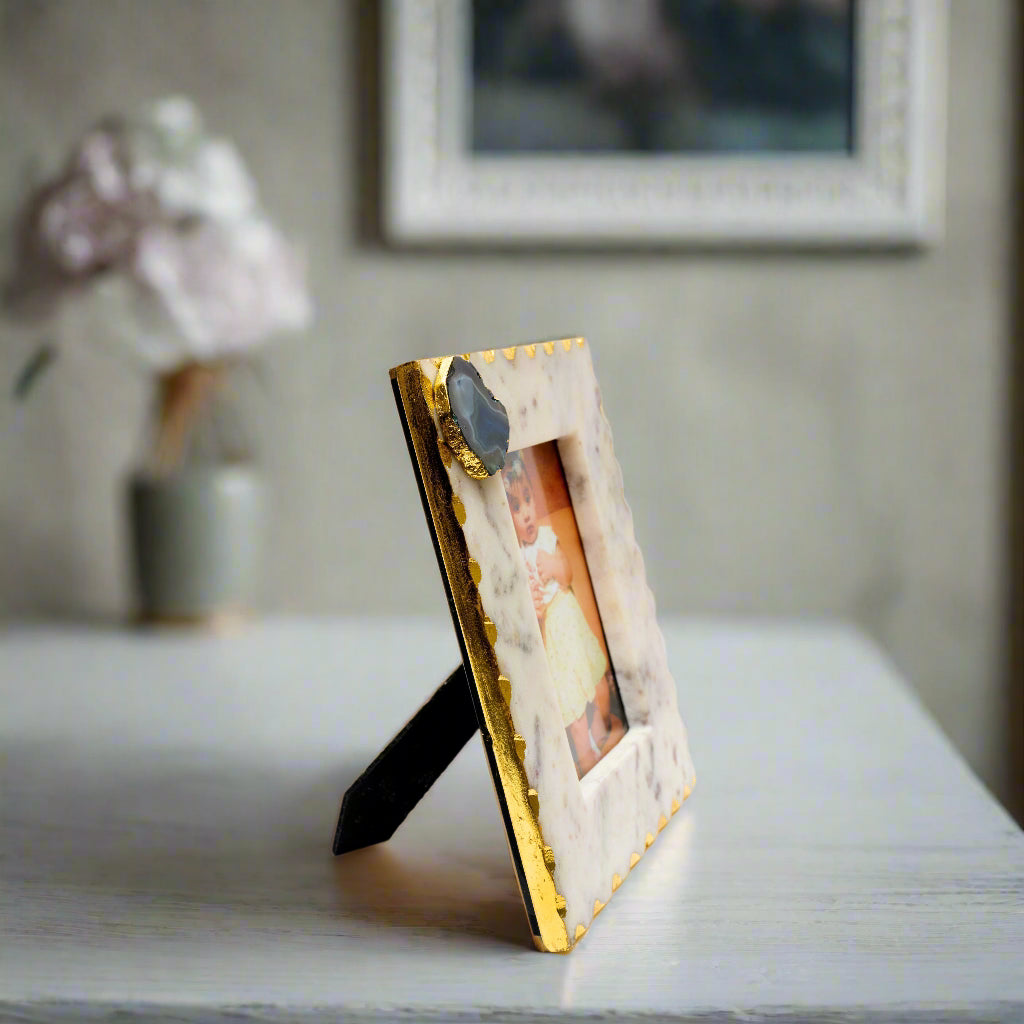 Decorative photo frame with gold accents and a white marble base on a white background
