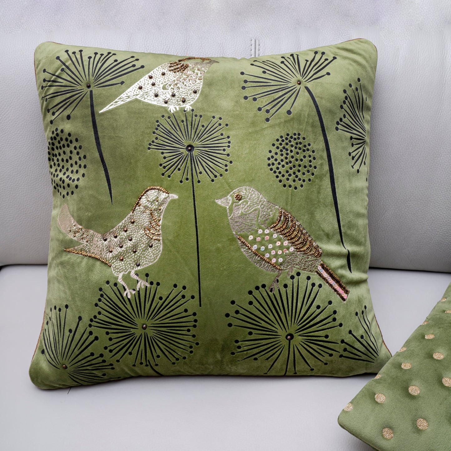 Green pillow with bird and dandelion design on a light gray background