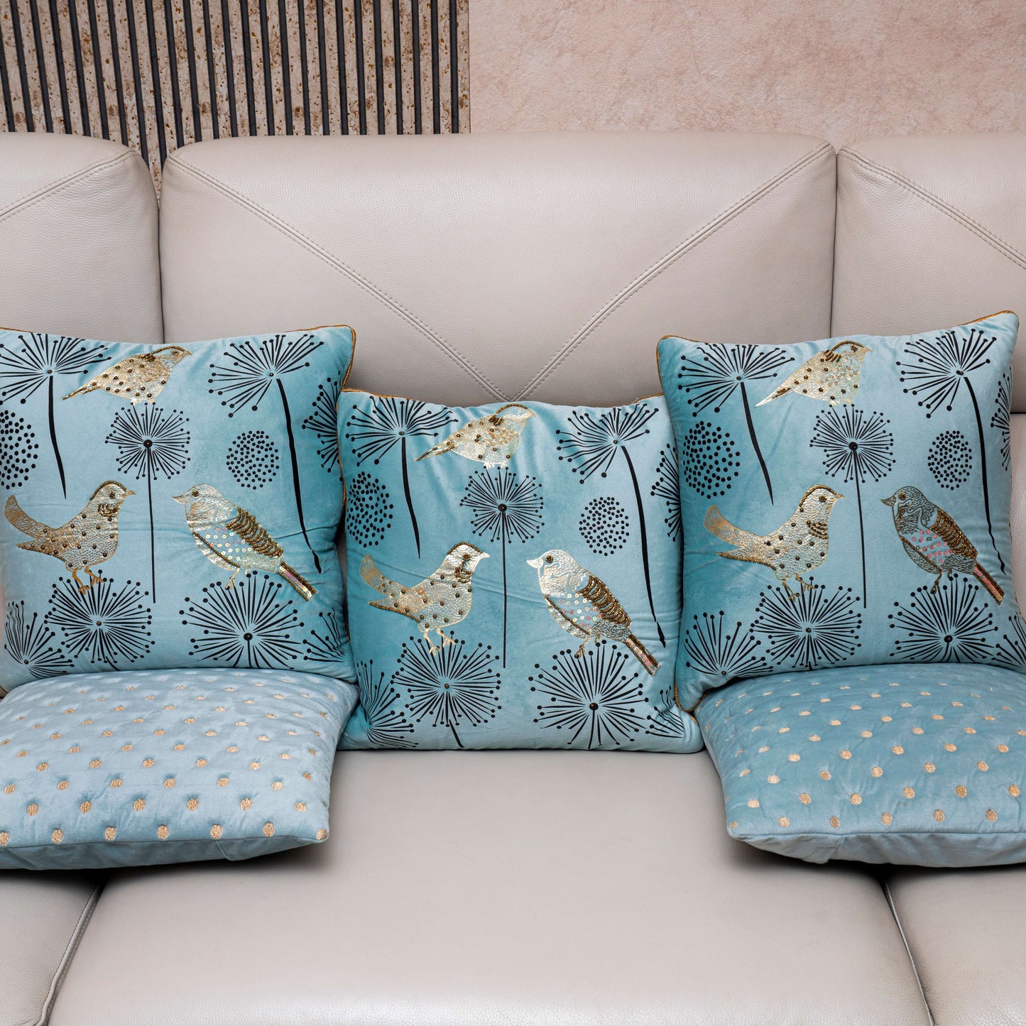 Set of decorative pillows with bird and floral patterns on a beige sofa.