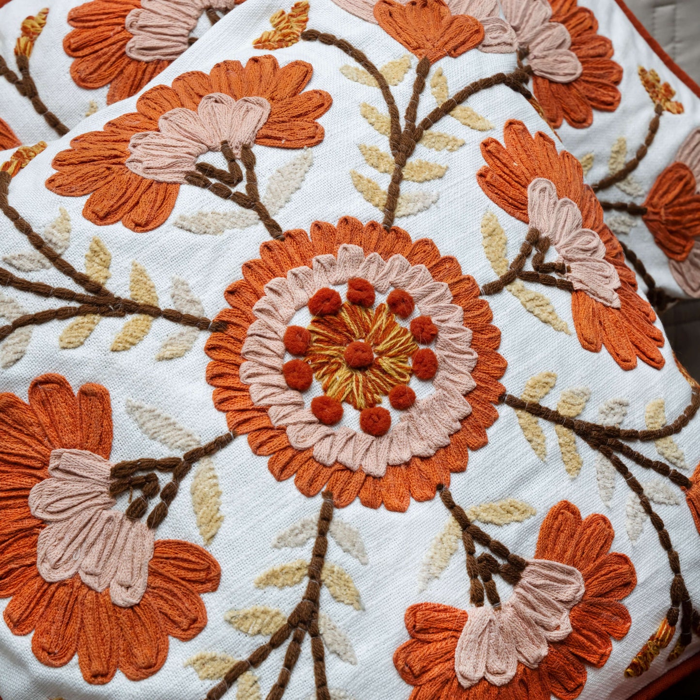 Close-up of a floral embroidery pattern on fabric with orange, pink, and brown colors.
