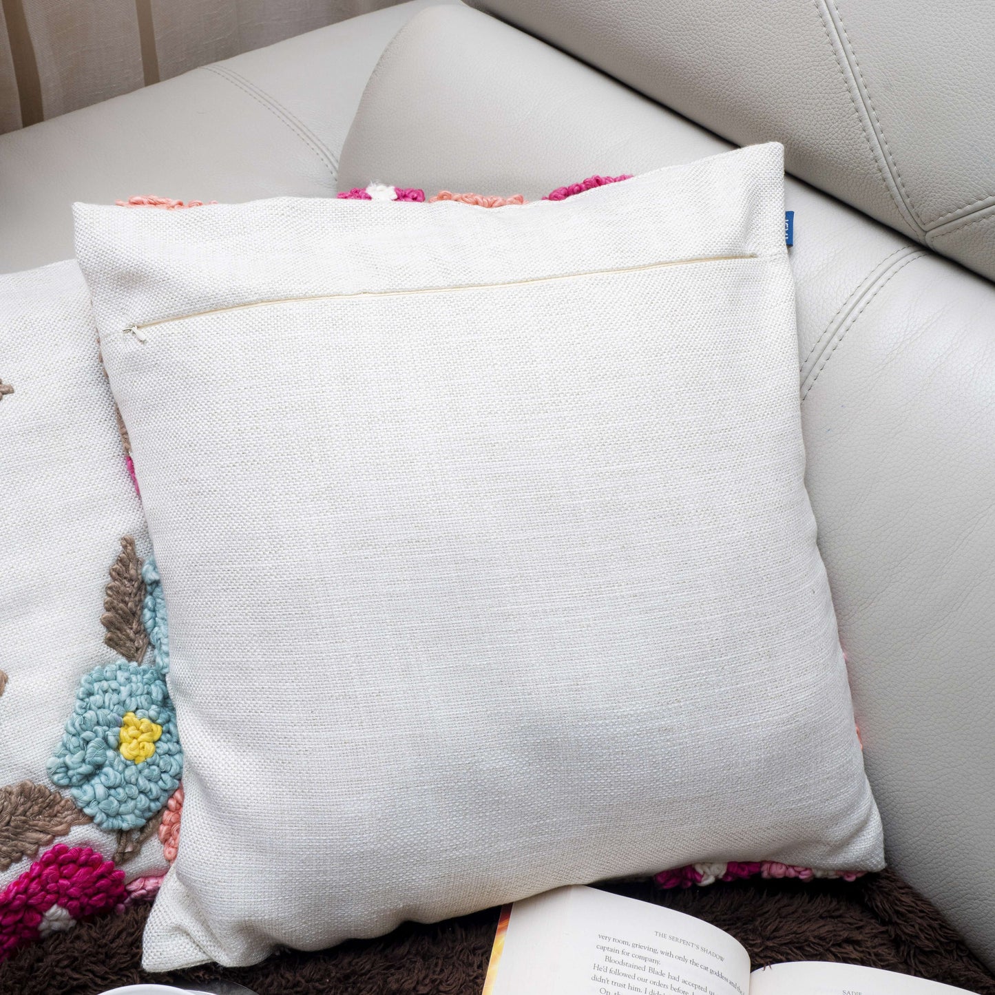 White pillow on a couch with a colorful blanket and book underneath