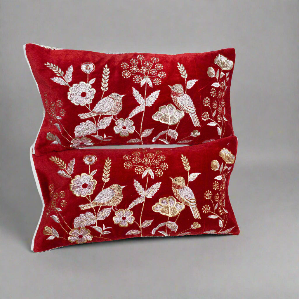 Two red pillows with gold floral and bird patterns on a white background