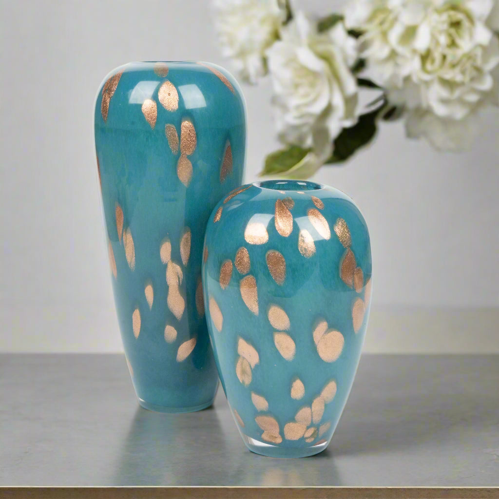 Two turquoise vases with gold leaf patterns on a reflective surface.