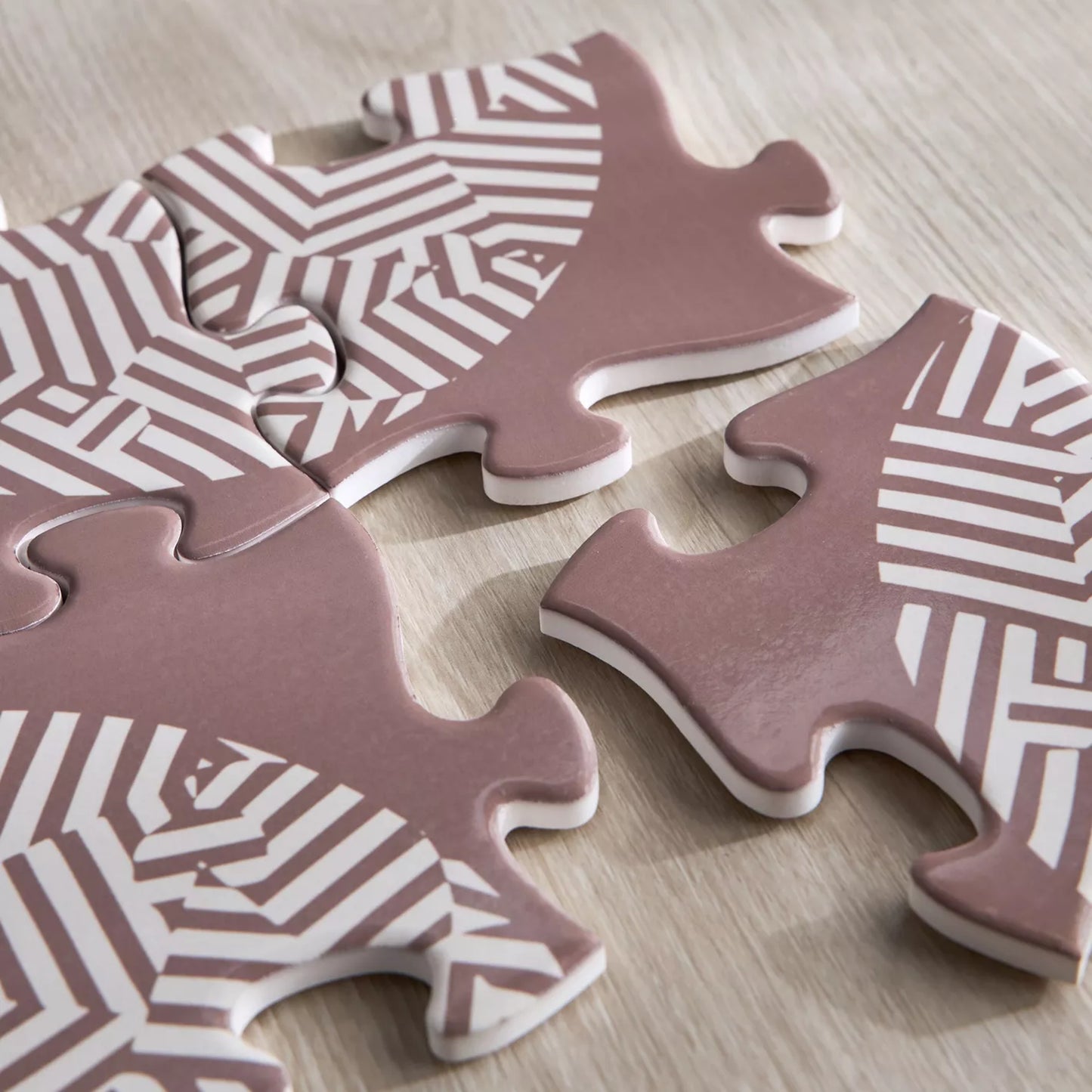 Pink puzzle pieces with white geometric patterns on a wooden surface