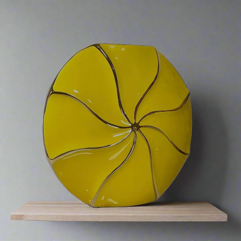 Yellow ceramic plate with a unique design on a wooden shelf against a gray wall