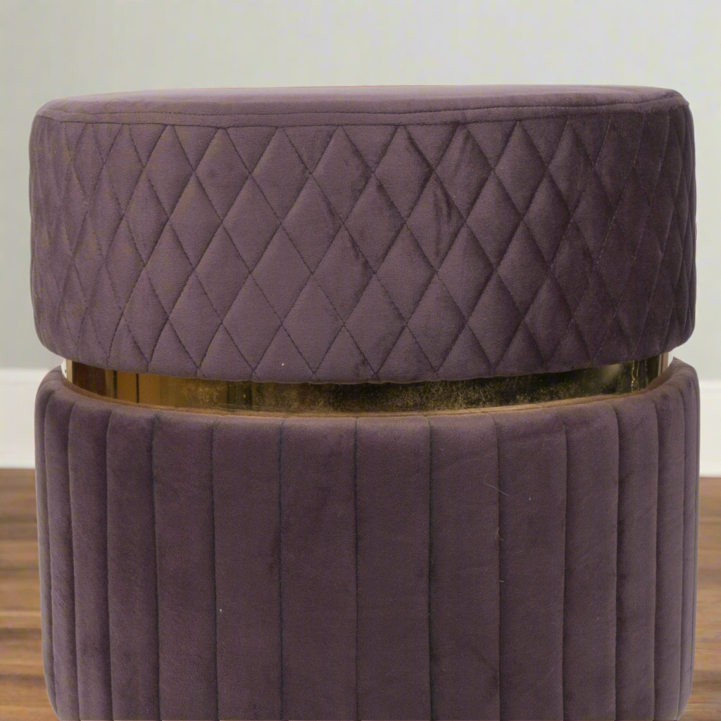 Purple quilted ottoman with a gold band on a wooden floor.