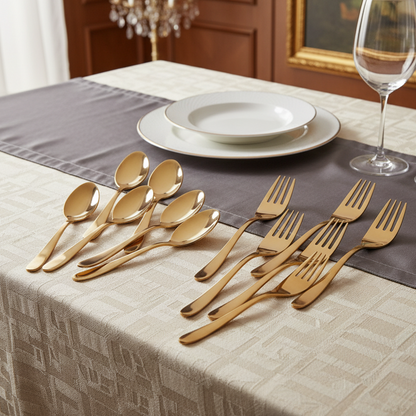 Set of gold flatware on a table with plates and a glass.