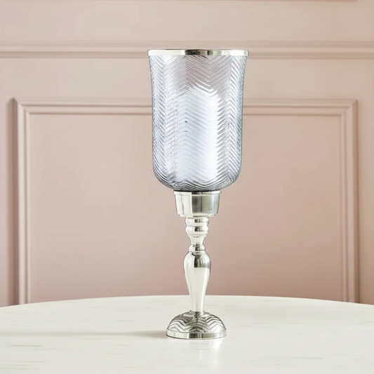Decorative candle holder with textured glass and silver base on a white surface with a pink paneled wall background.