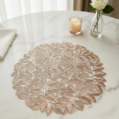 Decorative leaf-patterned placemat on a marble table with gold cutlery.
