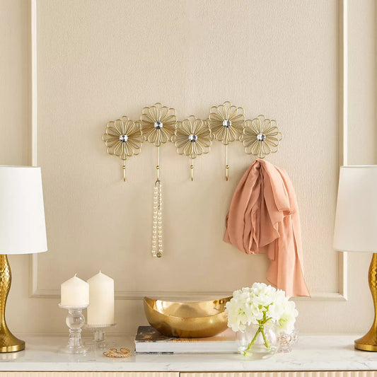 Decorative wall hooks with floral designs on a beige wall, with a scarf and small white flowers in the foreground.