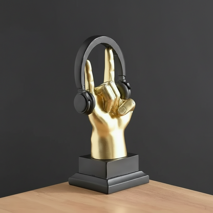 Gold hand sculpture holding black headphones on a wooden surface with a dark background