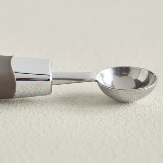 Metallic ice cream scoop on a light beige background