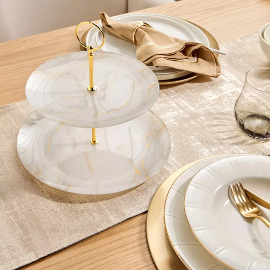 Two-tiered marble cake stand with gold accents on a dining table setting.