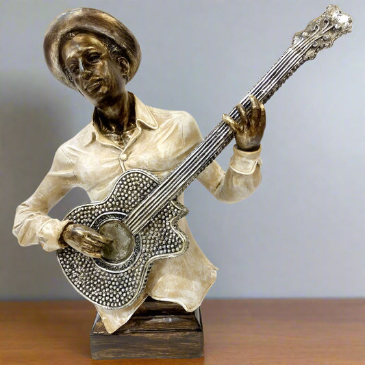 Bronze sculpture of a person playing an acoustic guitar on a wooden surface with a gray background