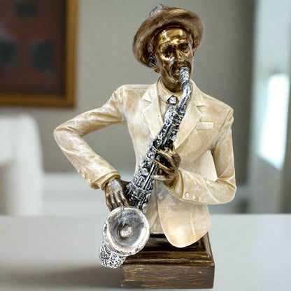 A vintage-style sculpture of a musician playing the saxophone, wearing a hat and suit. The sculpture is primarily in shades of white and gold with a focus on the saxophone details.