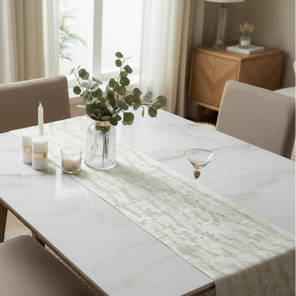 Dining table set with a vase of greenery, candles, and a decorative runner in a bright room.