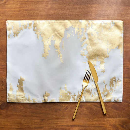 Gold and white abstract patterned placemat with gold fork and knife on a wooden surface
