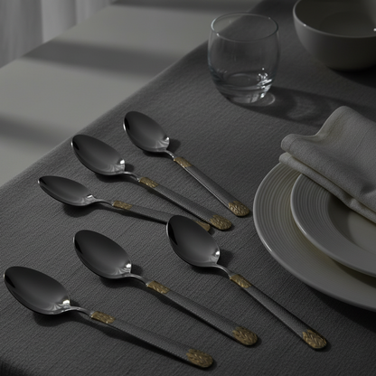 Set of black spoons on a gray tablecloth with a glass and bowl in the background.