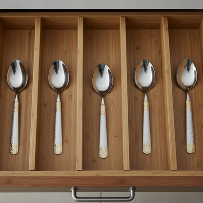 Set of six silver spoons with gold and white handles in a wooden drawer.