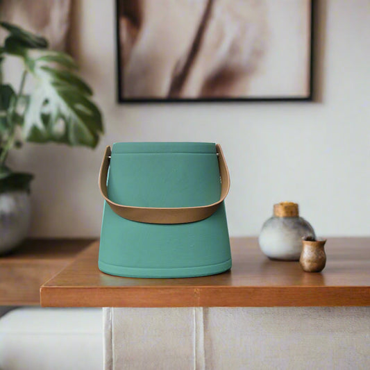 Green bucket with a brown handle on a dark tiled floor against a light wall.