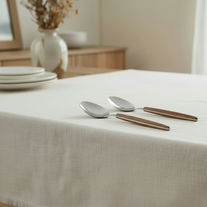 Two spoons on a white tablecloth with a blurred background of a dining area.